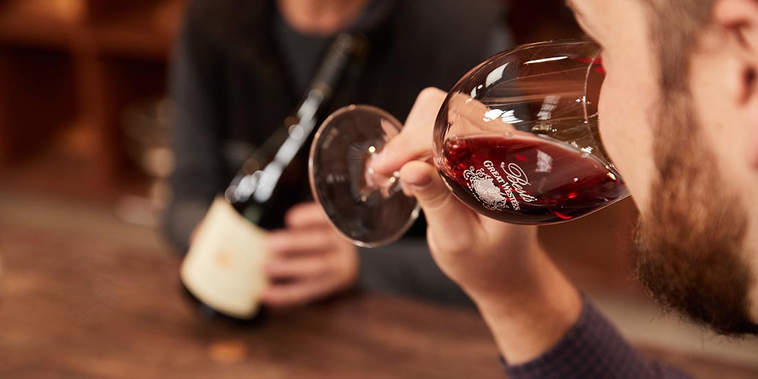 A man sipping wine and another person holding the wine bottle. 